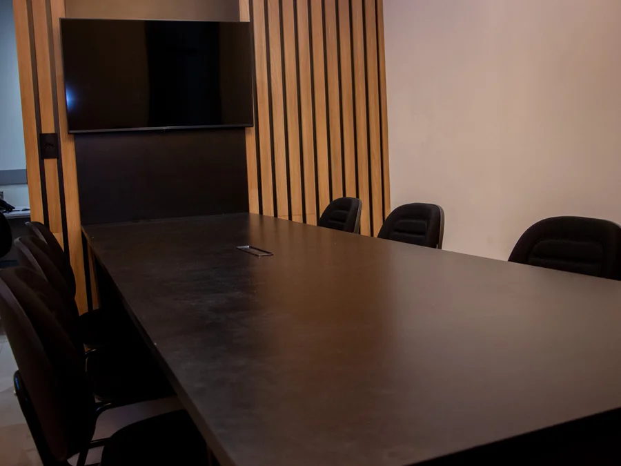 Sala de reunião do escritório, com mesa ampla e televisor para atendimentos